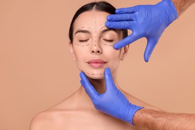 Doctor checking marks on woman's face for cosmetic surgery operation against beige background