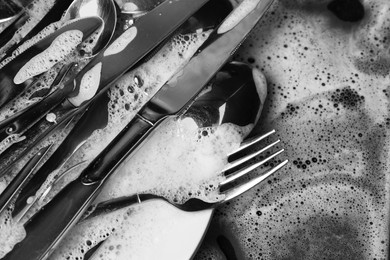 Washing silver spoons, forks and knives in foam, above view