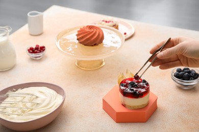 Photo of Food stylist creating composition with delicious dessert on table indoors, closeup