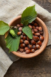 Photo of Tasty hazelnuts and green leaves on wooden table, top view. Healthy snack