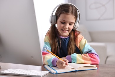 Photo of E-learning. Cute girl taking notes during online lesson at table indoors