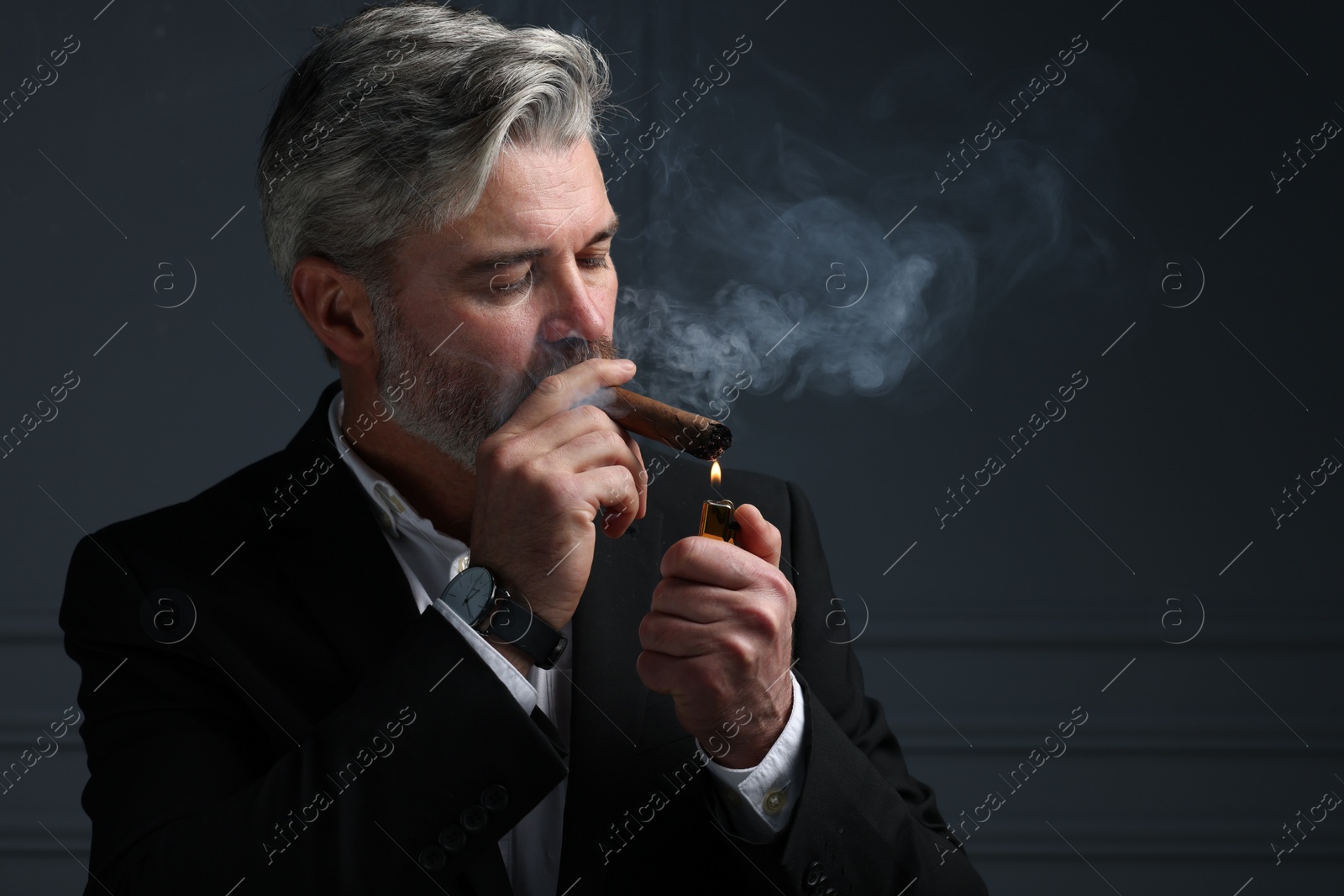 Photo of Bearded man lighting cigar on dark grey background. Space for text