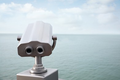 Photo of Metal tower viewer installed near sea, space for text. Mounted binoculars