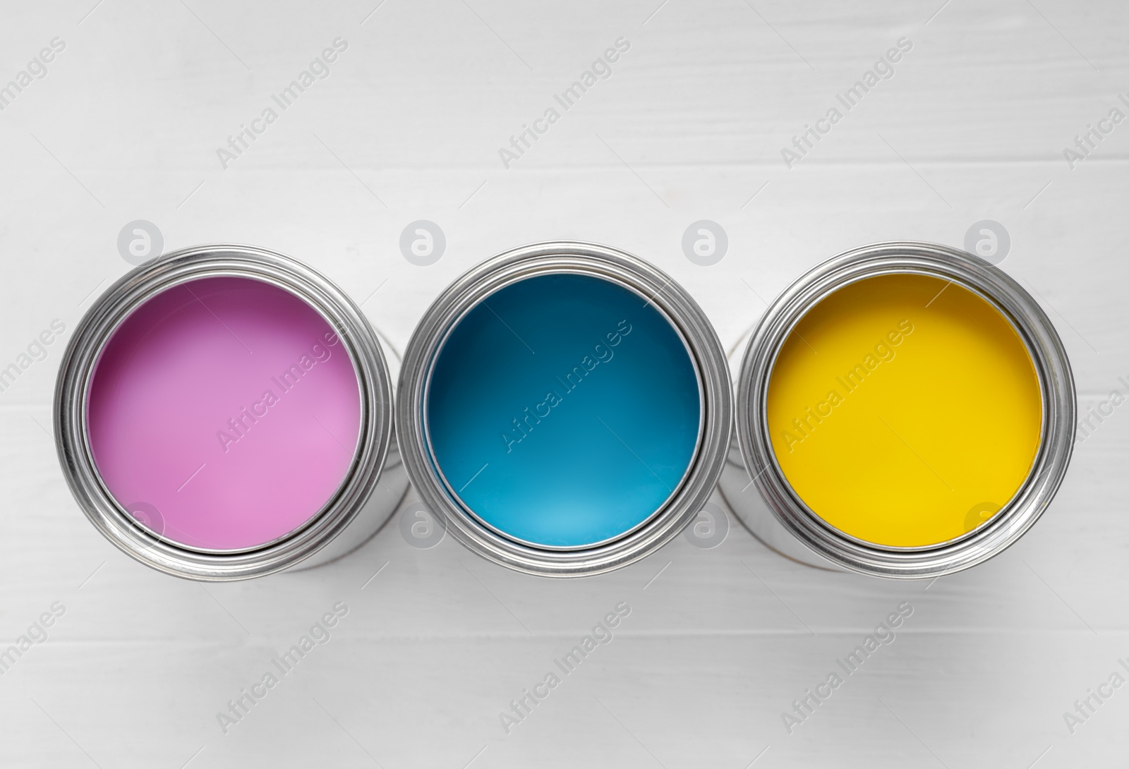 Photo of Cans of pink, light blue and yellow paints on white wooden table, flat lay