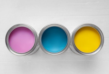 Cans of pink, light blue and yellow paints on white wooden table, flat lay