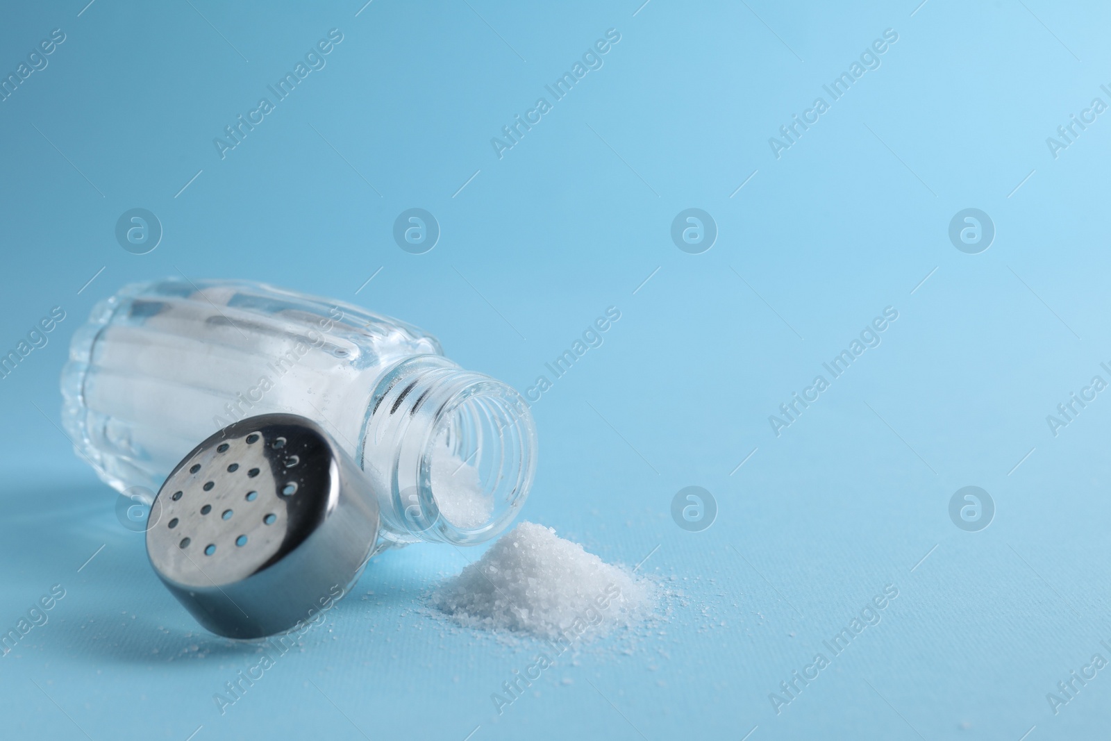 Photo of Organic white salt in shaker on light blue background, closeup. Space for text