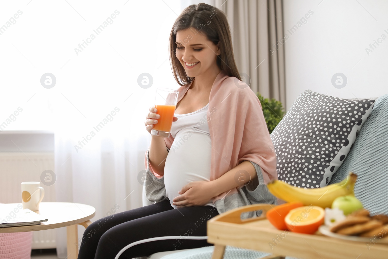 Photo of Young pregnant woman holding glass with juice at home
