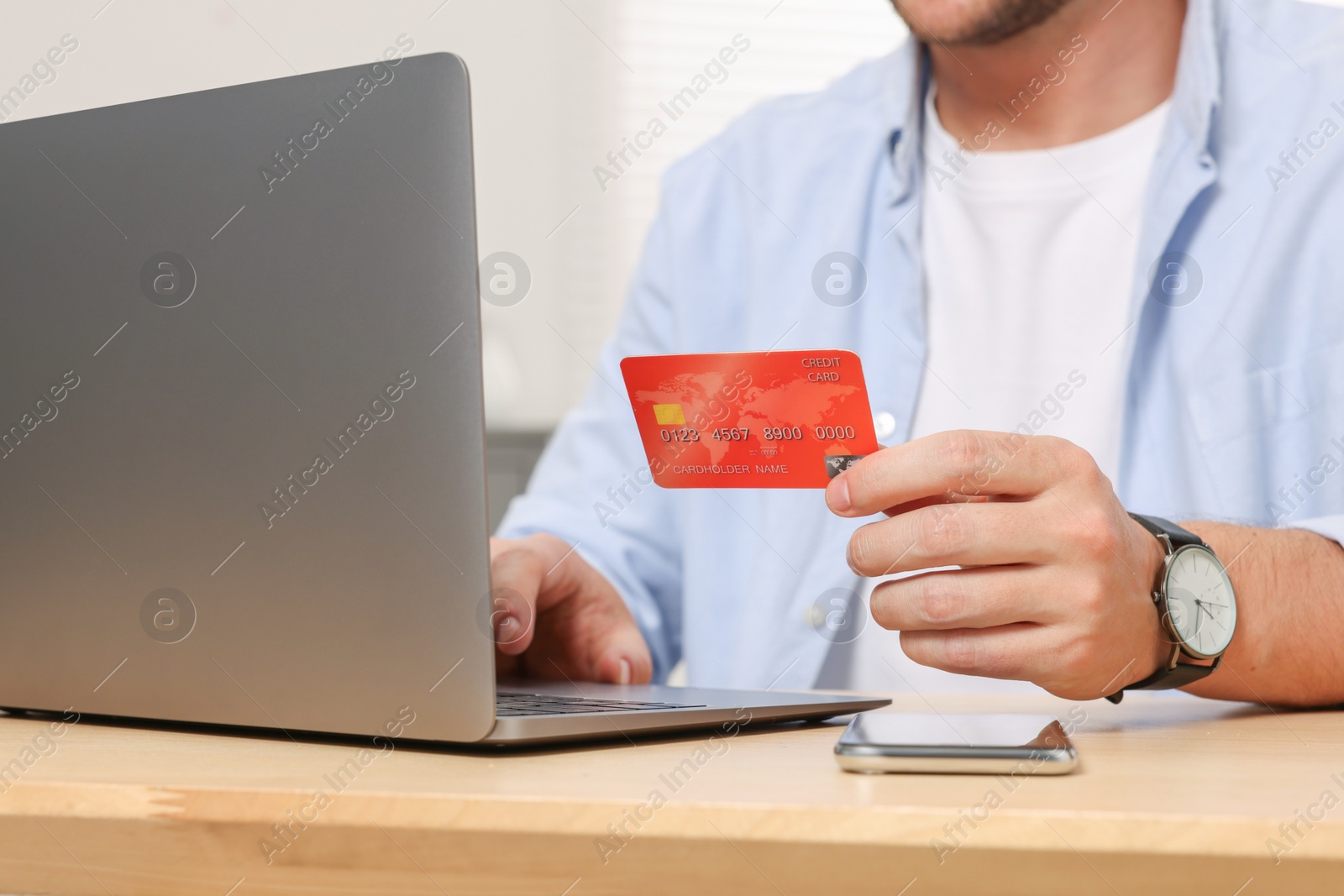 Photo of Man with credit card using laptop for online shopping at wooden table indoors, closeup