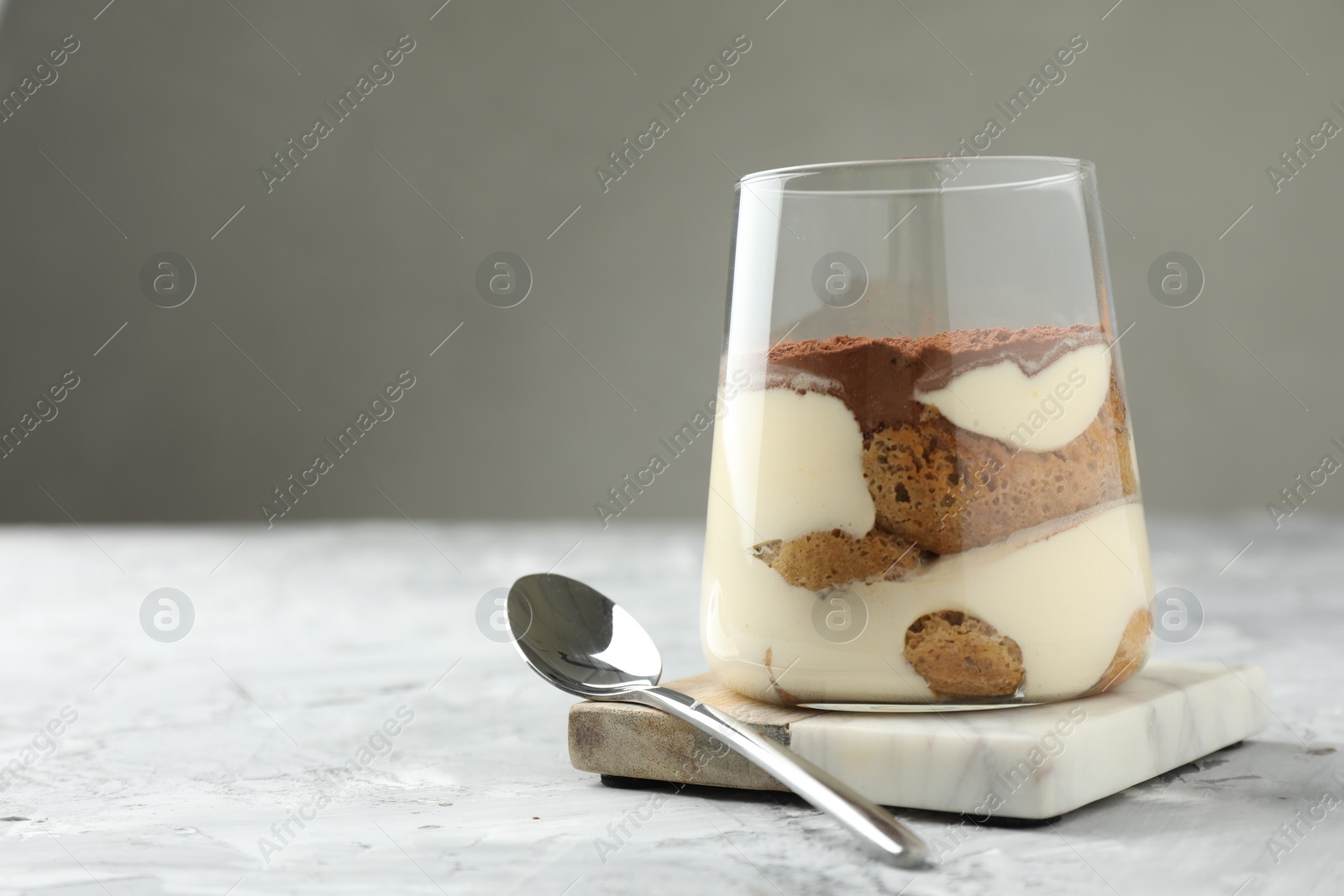 Photo of Delicious tiramisu in glass and spoon on grey textured table, space for text