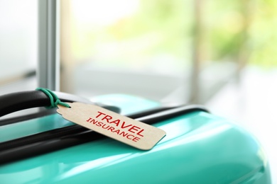 Photo of Stylish suitcase with travel insurance label on blurred background, closeup