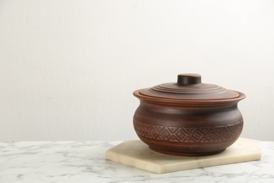 Photo of Brown clay pot on white marble table, space for text. Handmade utensil