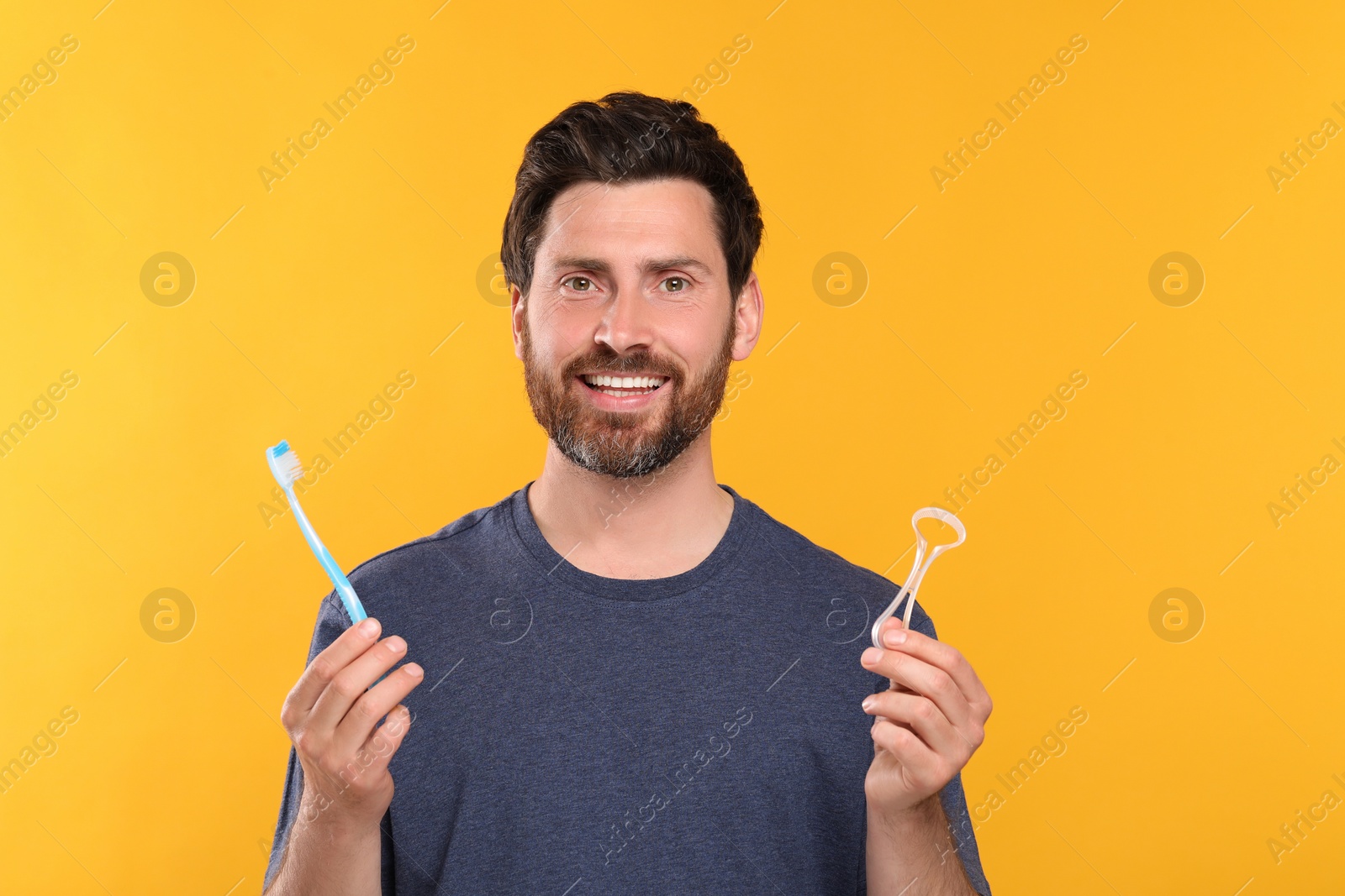 Photo of Happy man with tongue cleaner and plastic toothbrush on yellow background