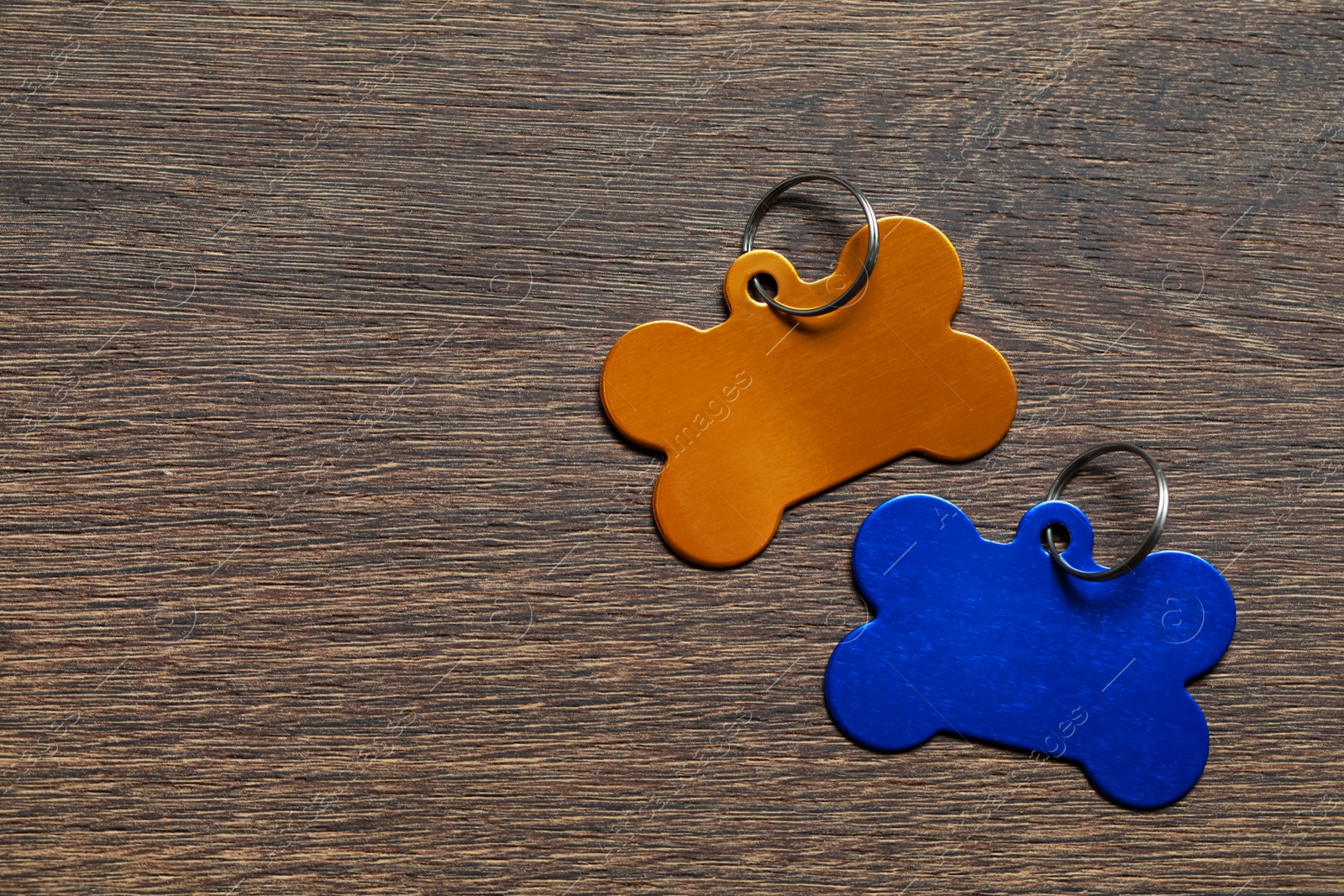 Photo of Color metal pet tags in shape of bones with ring on wooden table, flat lay. Space for text
