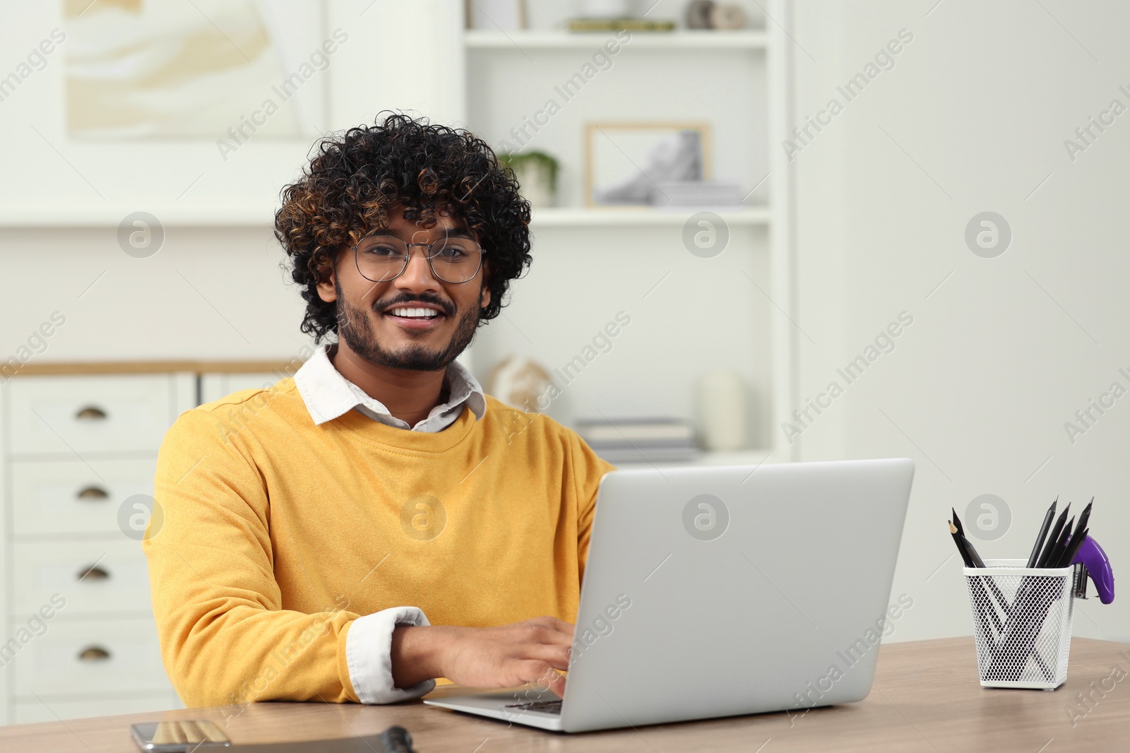 Photo of Handsome smiling man using laptop in room