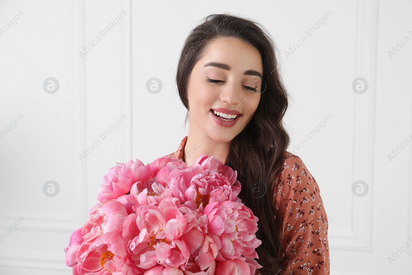 Photo of Beautiful young woman with bouquet of pink peonies near white wall