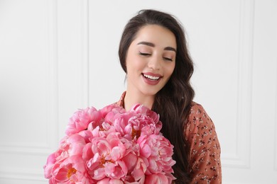 Photo of Beautiful young woman with bouquet of pink peonies near white wall