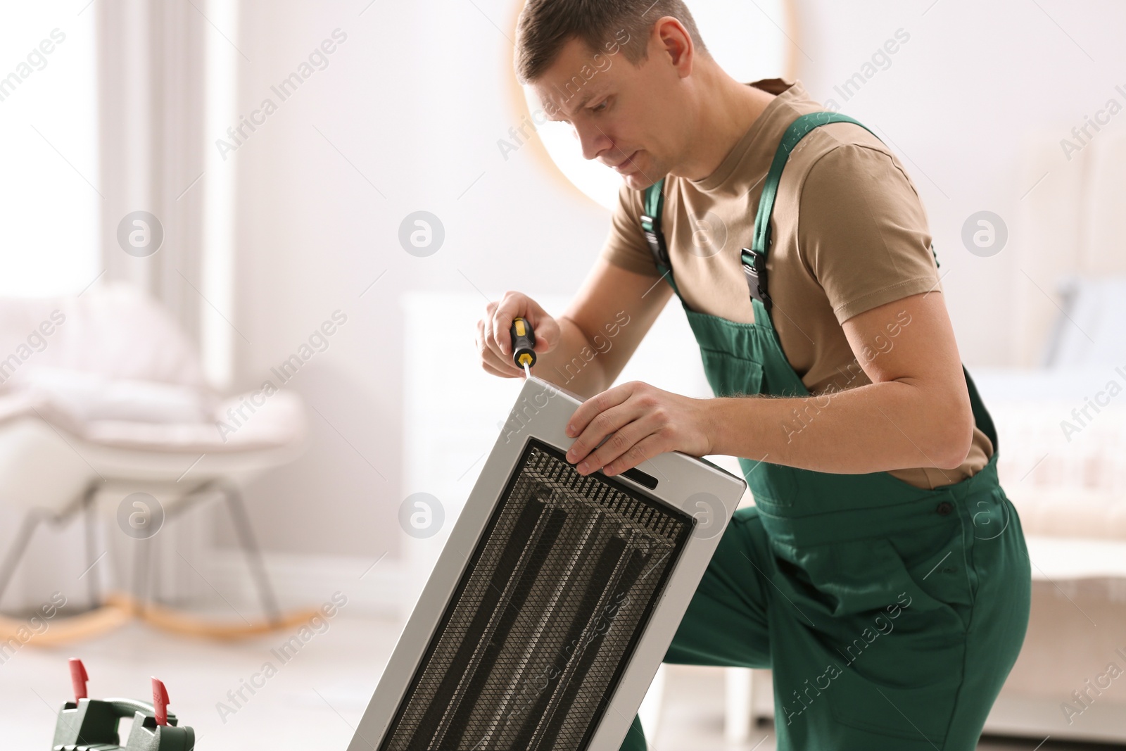 Photo of Professional technician repairing electric ultrared heater with screwdriver indoors, space for text