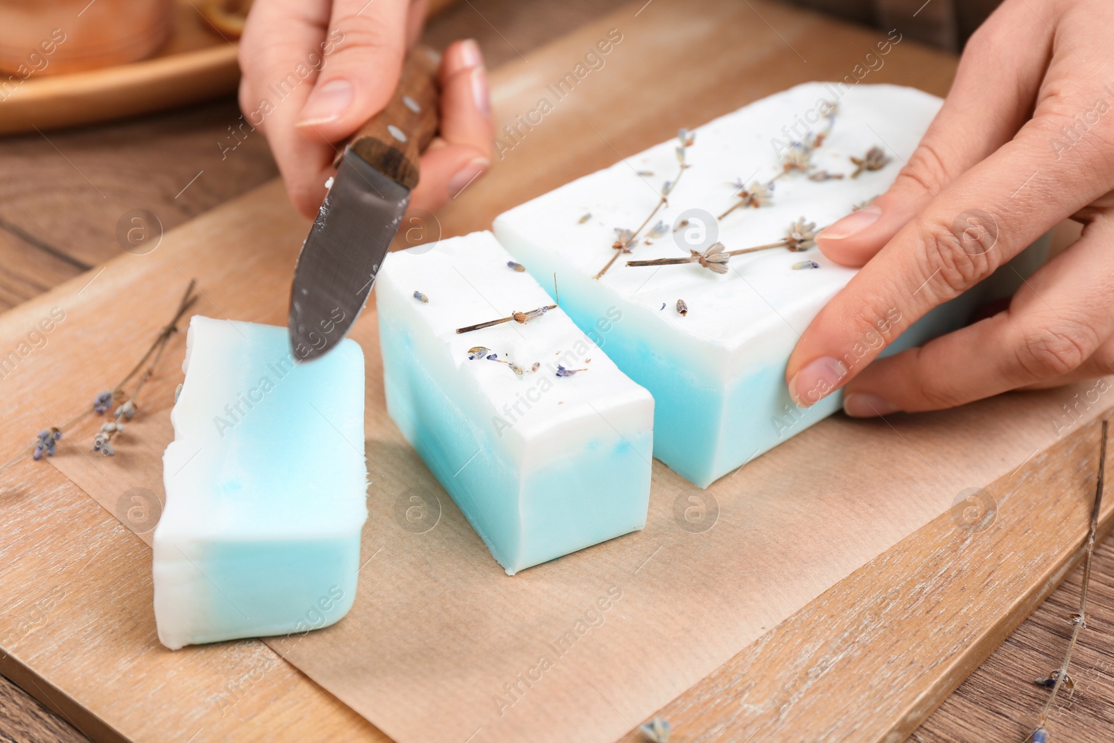 Photo of Woman cutting natural handmade soap on wooden table, closeup