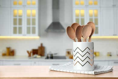 Image of Holder with spoons on wooden table and blurred view of stylish kitchen interior. Mockup for design