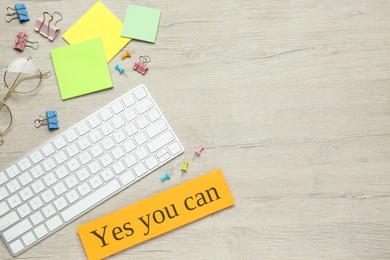 Photo of Note with motivational quote Yes you can, computer keyboard and office stationery on white wooden background, flat lay. Space for text