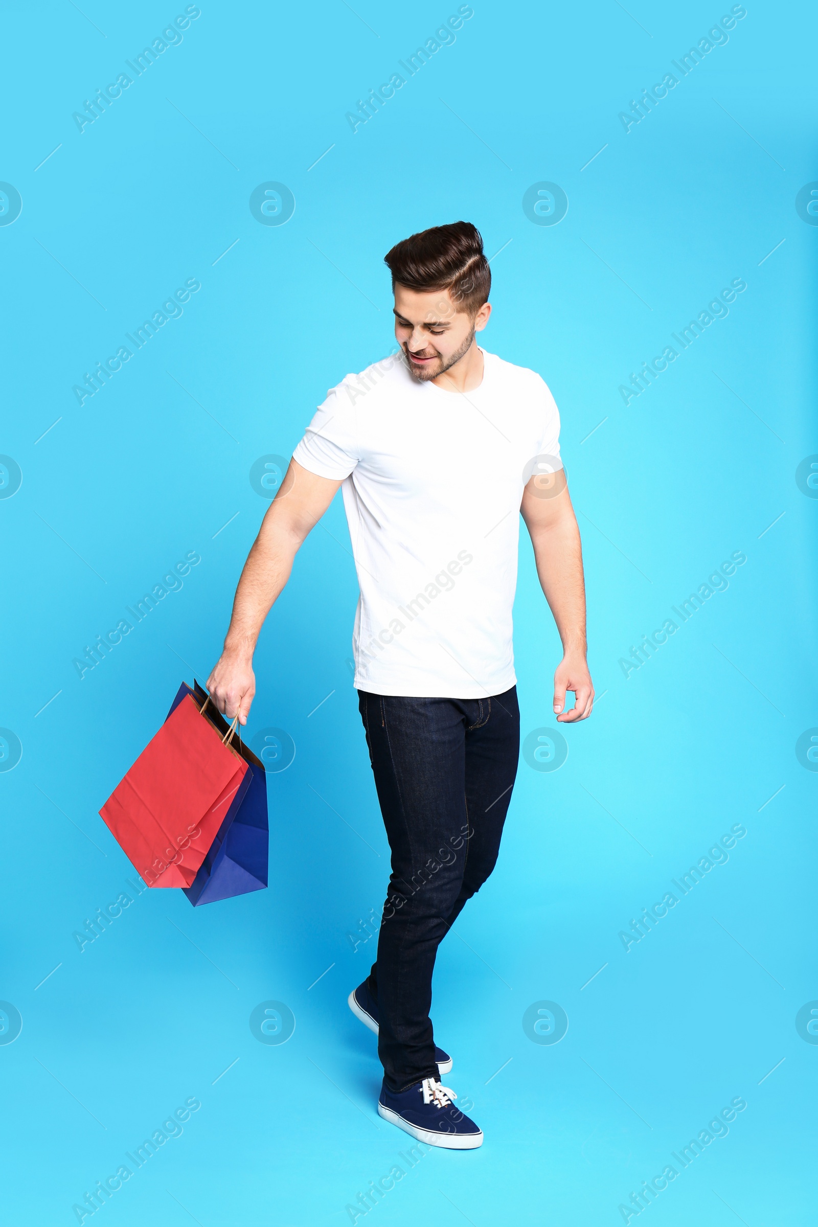 Photo of Full length portrait of young man with paper bags on blue background