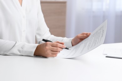 Photo of Businesswoman working with contract at white table in office, closeup