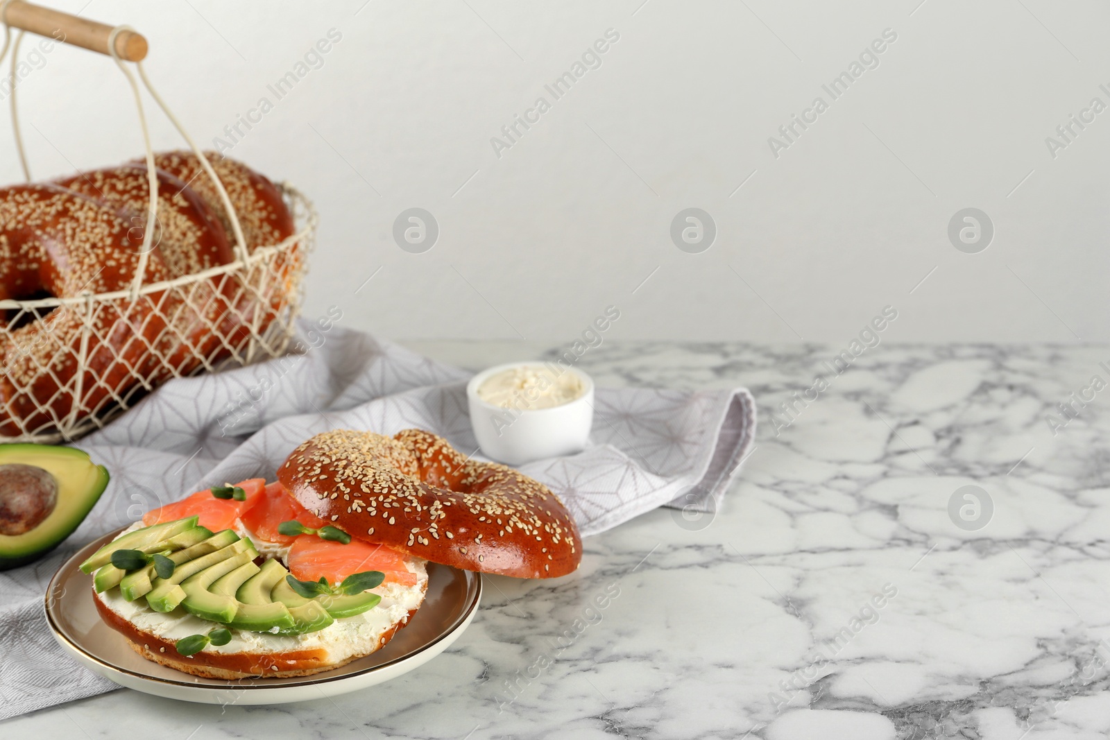 Photo of Delicious bagel with cream cheese, salmon, avocado and microgreens on white marble table. Space for text