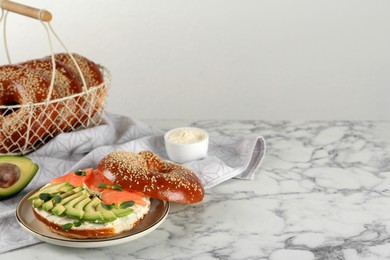 Photo of Delicious bagel with cream cheese, salmon, avocado and microgreens on white marble table. Space for text