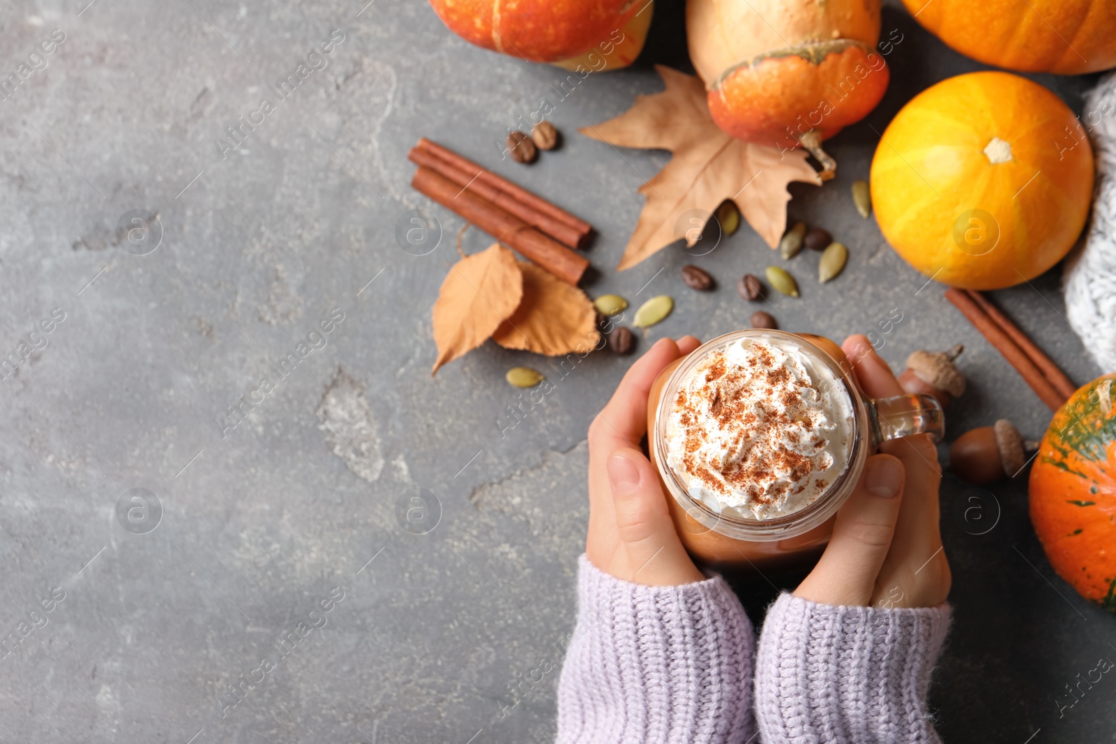 Photo of Woman holding mason jar of tasty pumpkin spice latte on gray table, flat lay with space for text