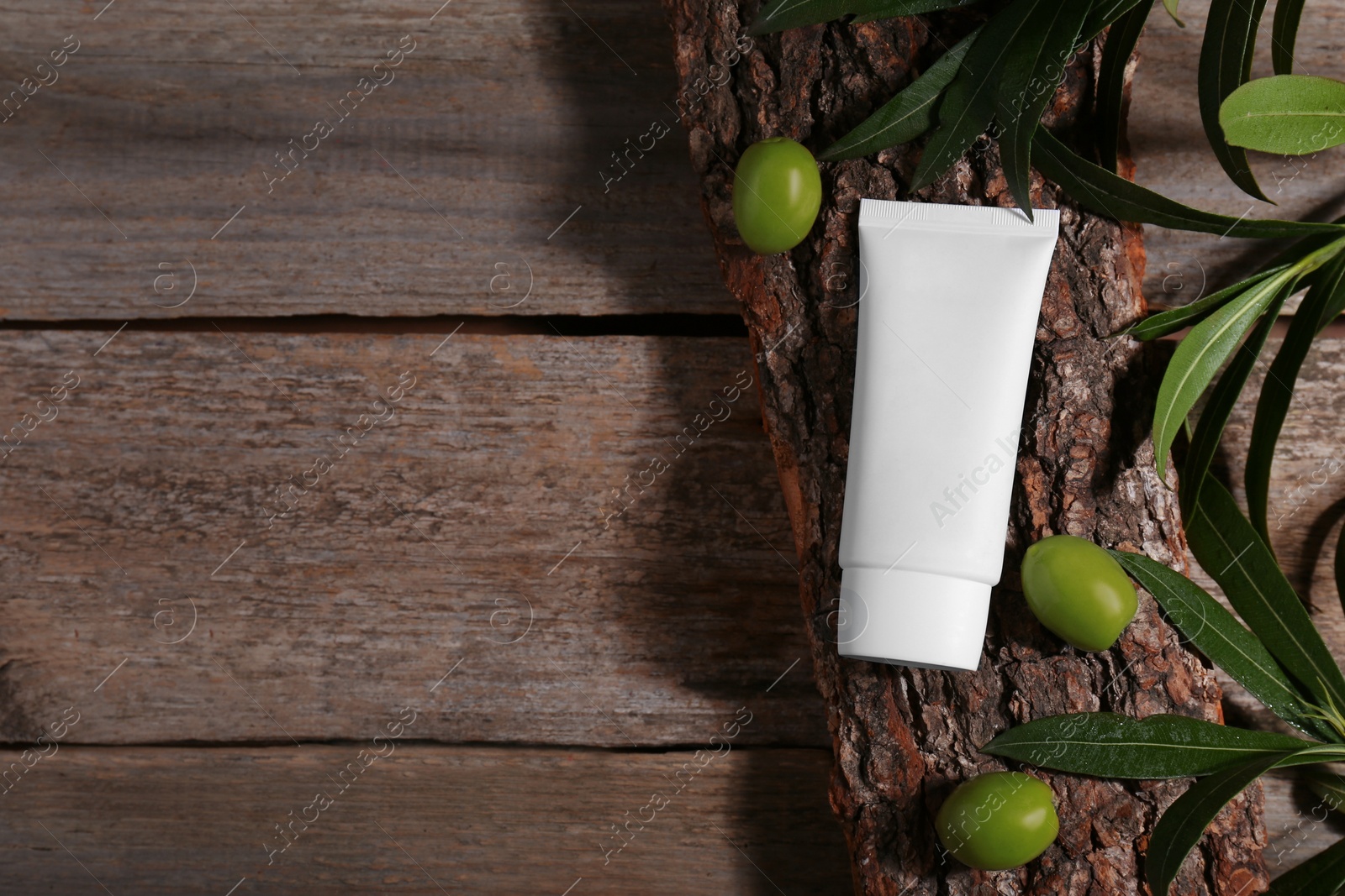 Photo of Tube of cream, olives and leaves on wooden table, flat lay. Space for text