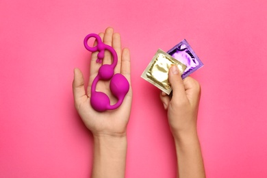 Photo of Woman with anal balls beads and condoms on pink background, top view. Sex game