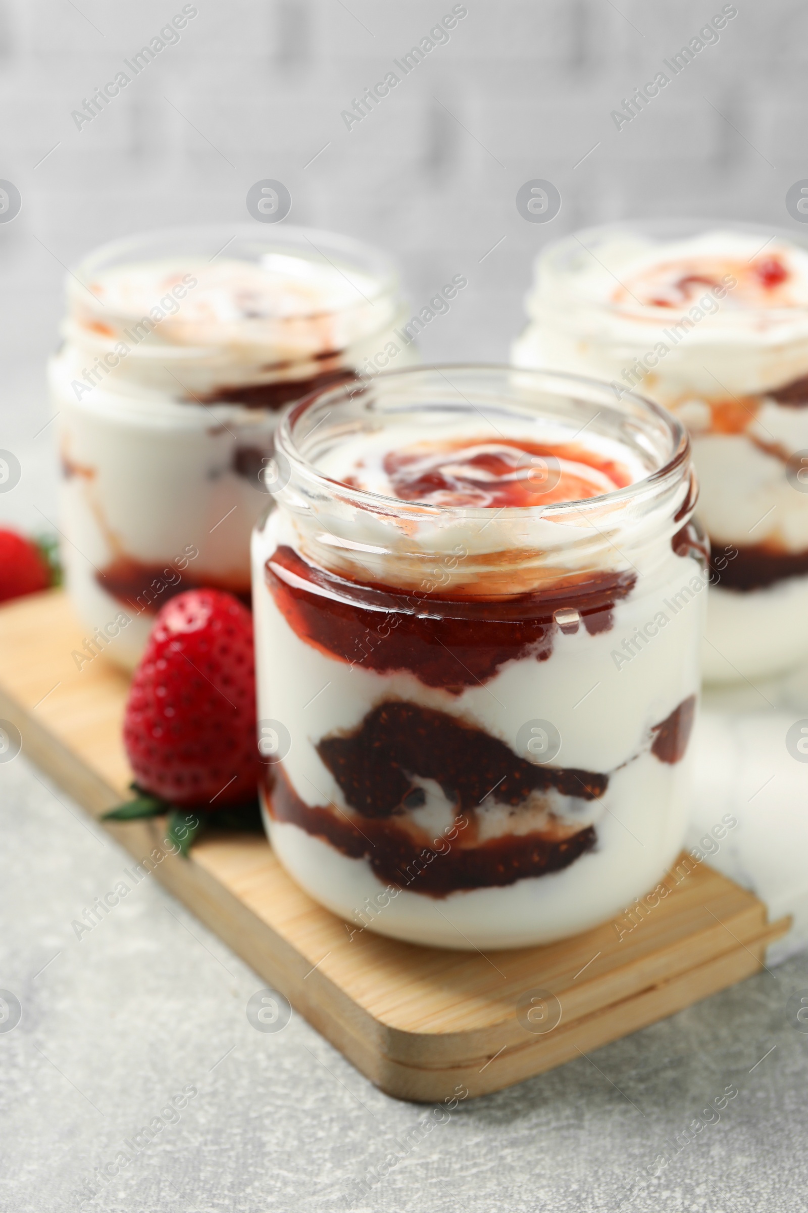 Photo of Tasty yoghurt with jam and strawberry on grey table, closeup