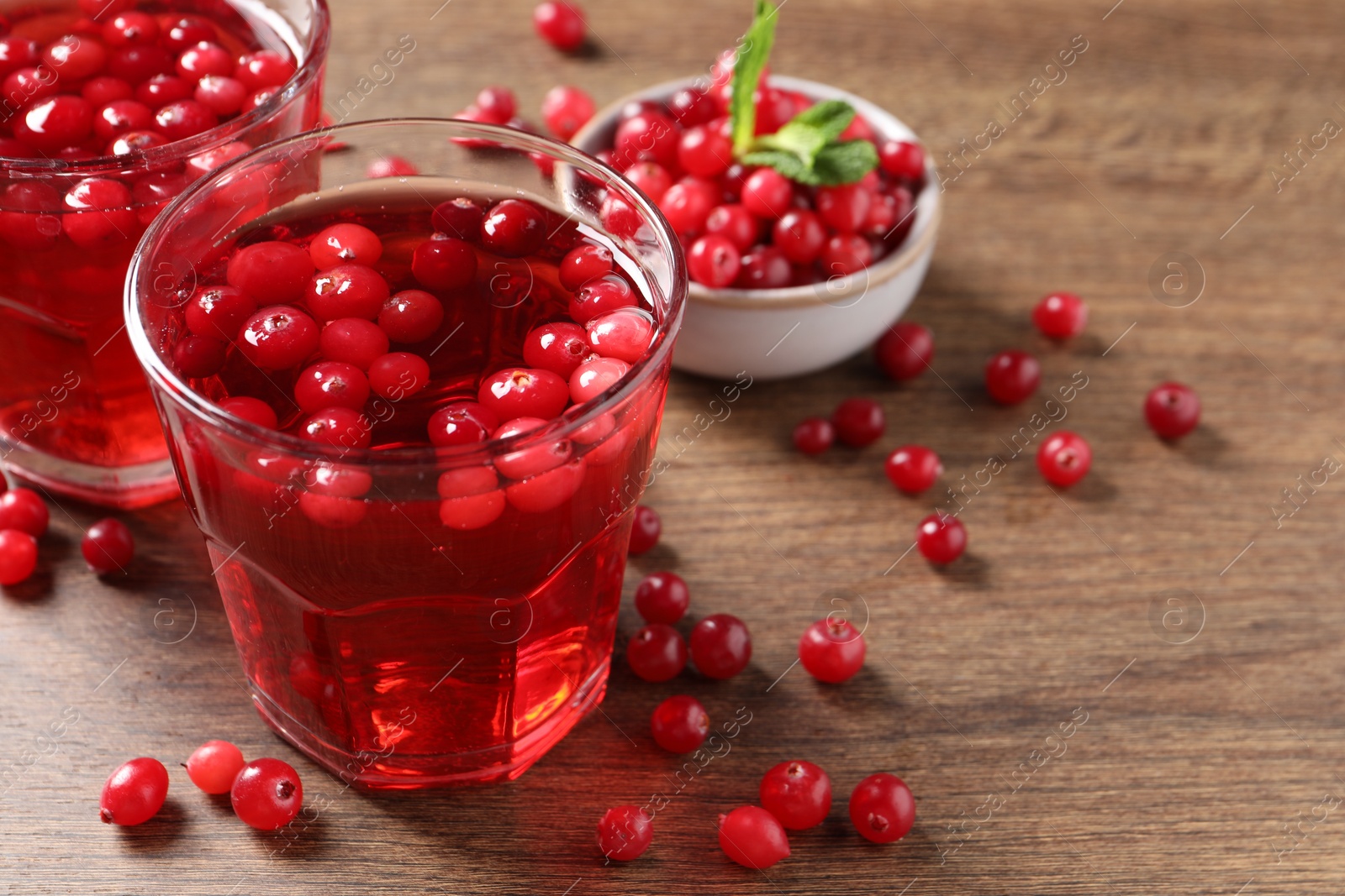 Photo of Tasty cranberry juice in glasses and fresh berries on wooden table, closeup. Space for text