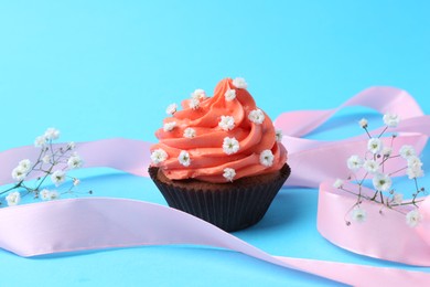 Delicious cupcake with bright cream and flowers on light blue background