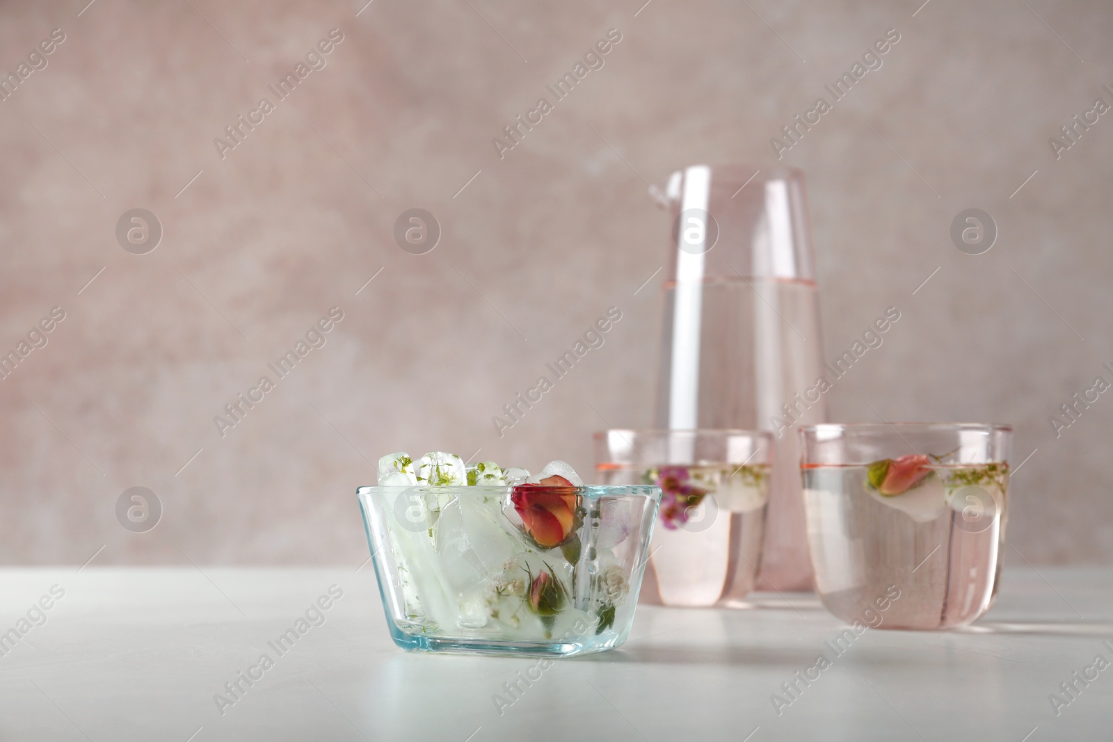 Photo of Bowl with floral ice cubes and glasses of water on table