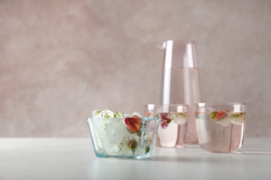 Bowl with floral ice cubes and glasses of water on table