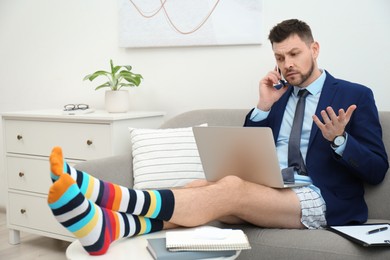 Photo of Businessman in shirt, underwear and funny socks talking on phone during video call at home