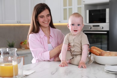 Photo of Happy young woman and her cute little baby spending time together in kitchen