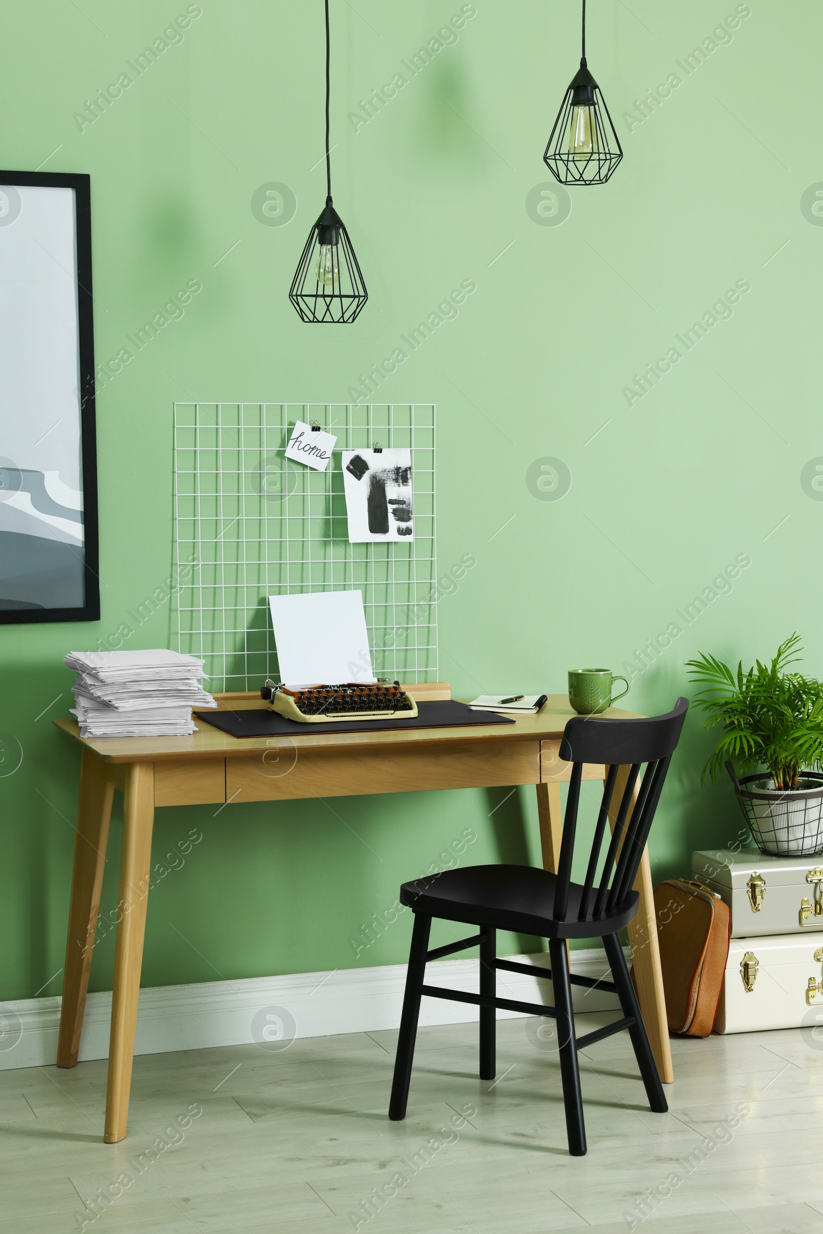 Photo of Typewriter, stack of papers and mood board on wooden table near pale green wall. Writer's workplace