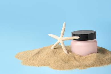 Jar with cream and starfish on sand against light blue background, space for text. Cosmetic product