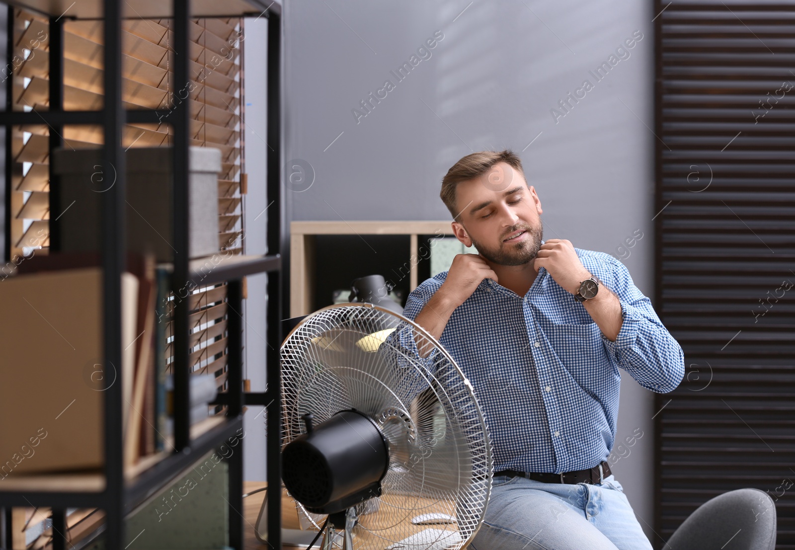 Photo of Man enjoying air flow from fan at workplace