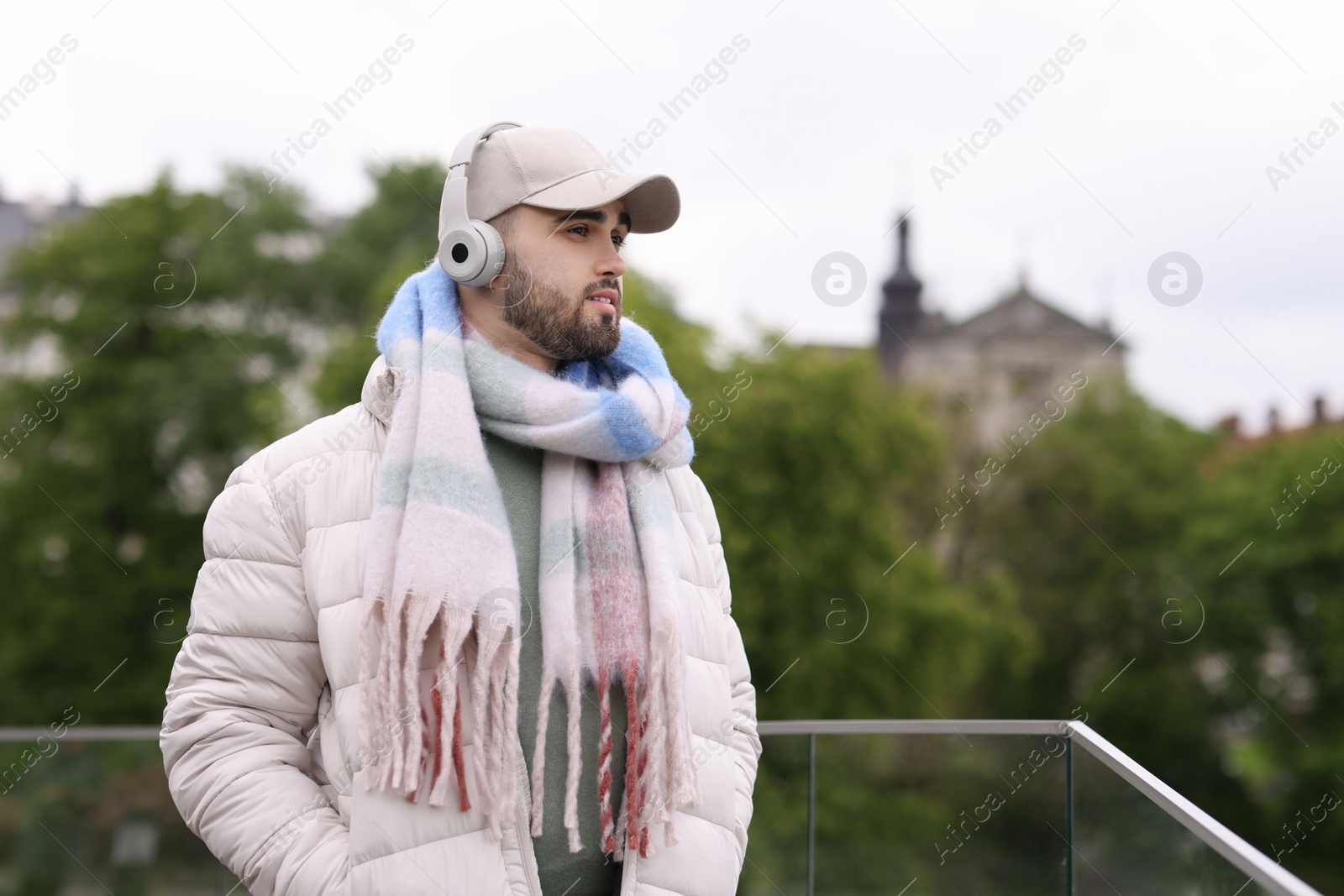 Photo of Handsome man in warm scarf and headphones outdoors. Space for text