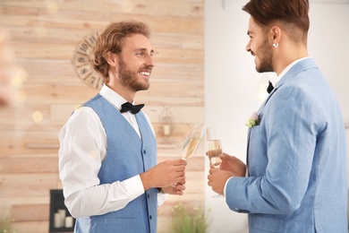 Happy newlywed gay couple with glasses of champagne at home