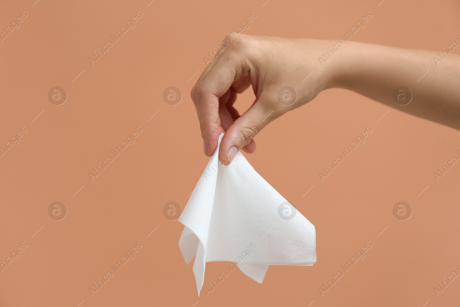 Photo of Woman holding paper tissue on light brown background, closeup