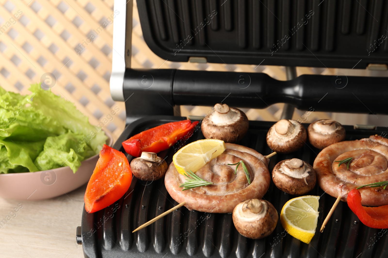 Photo of Electric grill with homemade sausages, bell pepper and mushrooms on table, closeup