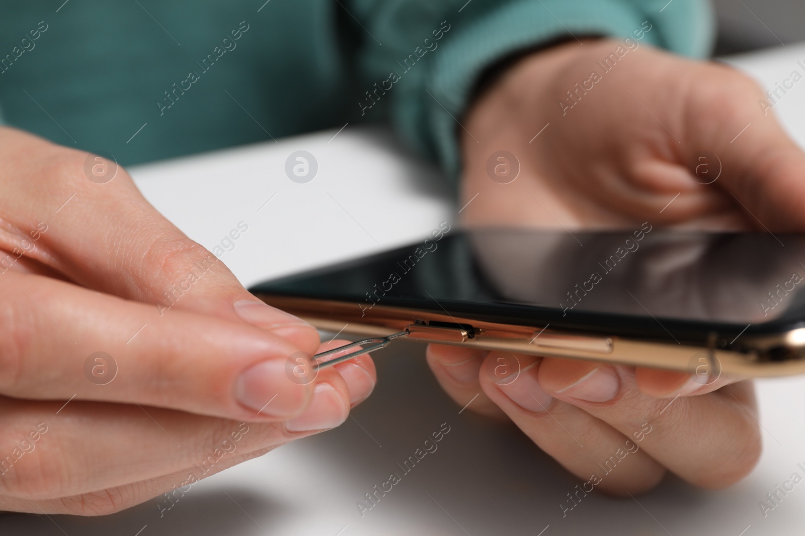 Photo of Woman with ejector opening SIM card tray in smartphone at white table, closeup