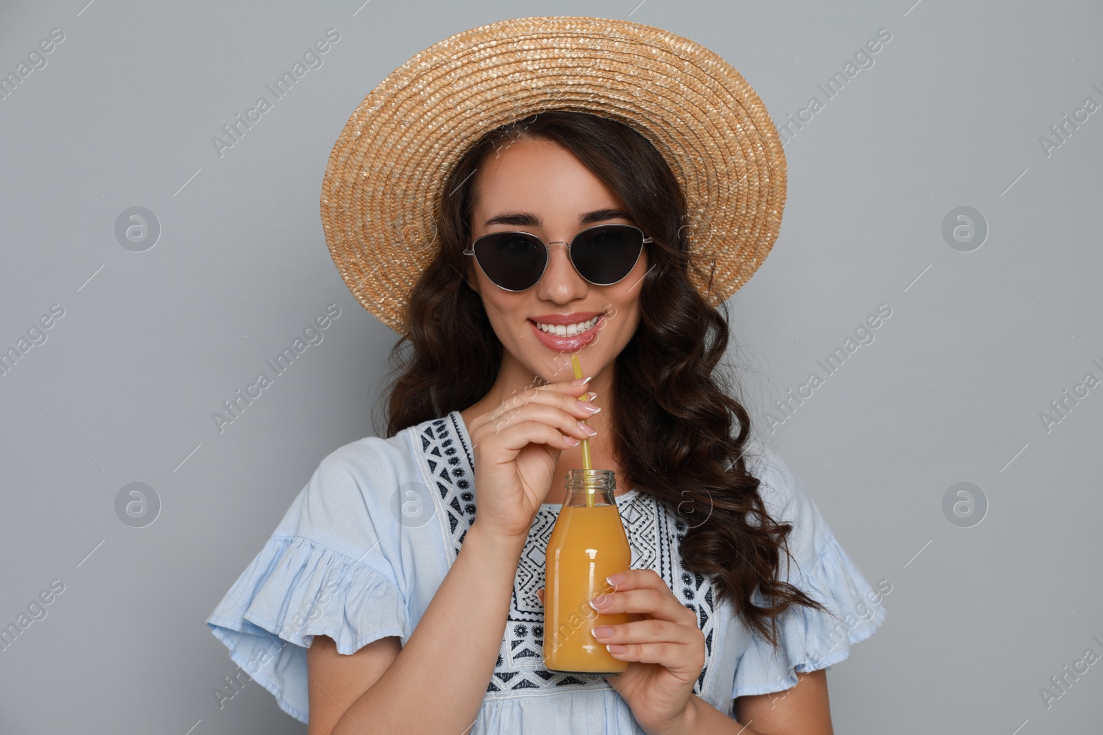 Photo of Beautiful young woman with straw hat and bottle of refreshing drink on light grey background