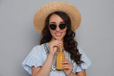 Beautiful young woman with straw hat and bottle of refreshing drink on light grey background