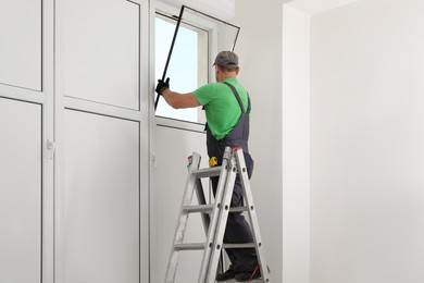 Worker on folding ladder installing window indoors