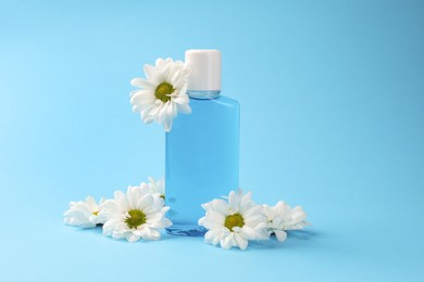 Photo of Fresh mouthwash in bottle and flowers on light blue background